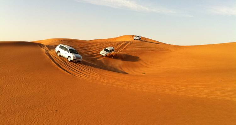 Tres vehículos 4x4 descienden por empinadas dunas de arena naranja durante una aventura de saltos en las dunas del desierto.
