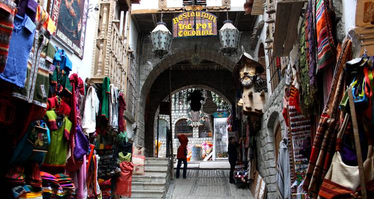 Los puestos de textiles coloridos se alinean en un callejón histórico bajo un arco de piedra en un distrito de mercado boliviano.