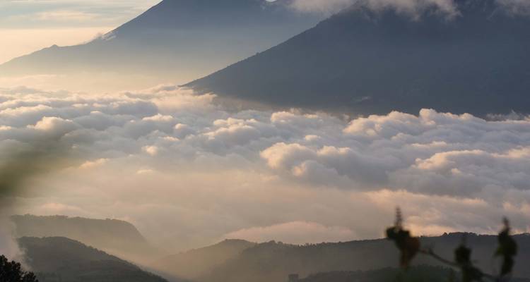 Mar de nubes iluminado por la cálida luz del amanecer con picos de volcanes emergiendo sobre las ondulantes crestas.