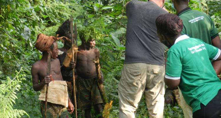 Les touristes interagissent avec les chasseurs locaux vivant en forêt portant des lances au milieu d'une végétation verte dense.