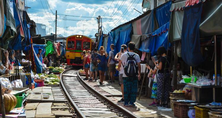 Mercado ferroviario concurrido con un tren amarillo brillante pasando entre los puestos mientras los compradores observan.