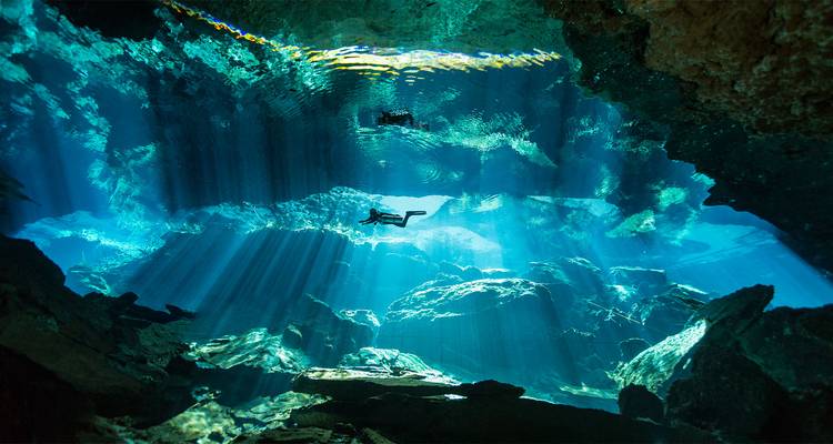 Freediver glijdt door zonnige lichtstralen in een kristalhelder cenote-grot