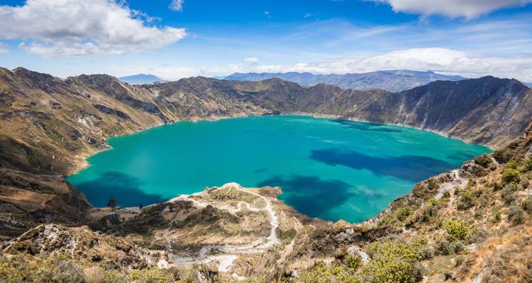 Las aguas de un turquesa brillante llenan la laguna del cráter de Quilotoa rodeada de picos andinos escarpados bajo un cielo despejado.