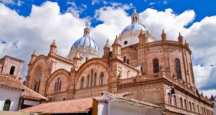 De grote koepels en bakstenen gevel van Cuenca's Nieuwe Kathedraal steken hoog uit onder fluffy witte wolken.