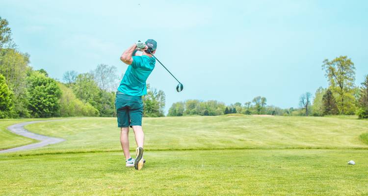 Golfista en mitad del swing en un hermoso green bajo un cielo azul despejado.