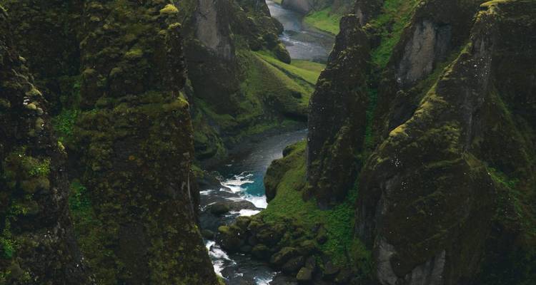 Deep moss-covered canyon with a winding river flowing through steep green cliffs