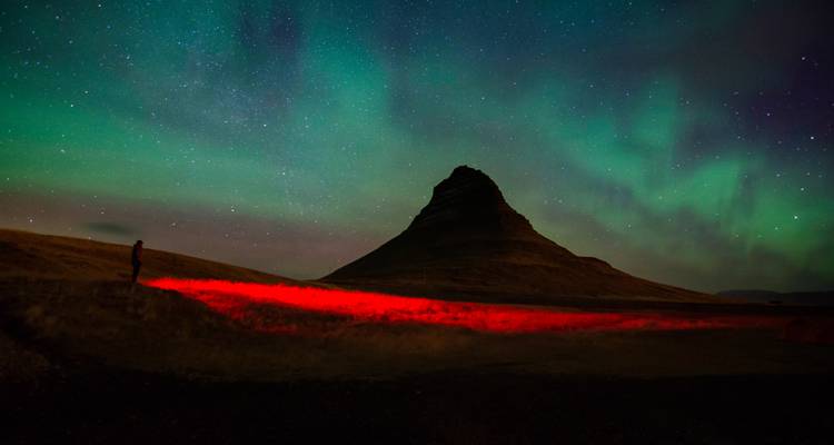 Northern lights dancing over Kirkjufell mountain with red-lit foreground