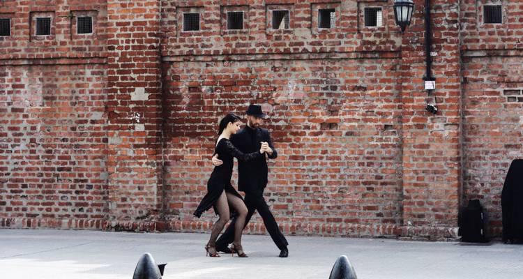 Pareja de tango actuando con pasión frente a una pared de ladrillos rojos rústica en Buenos Aires.