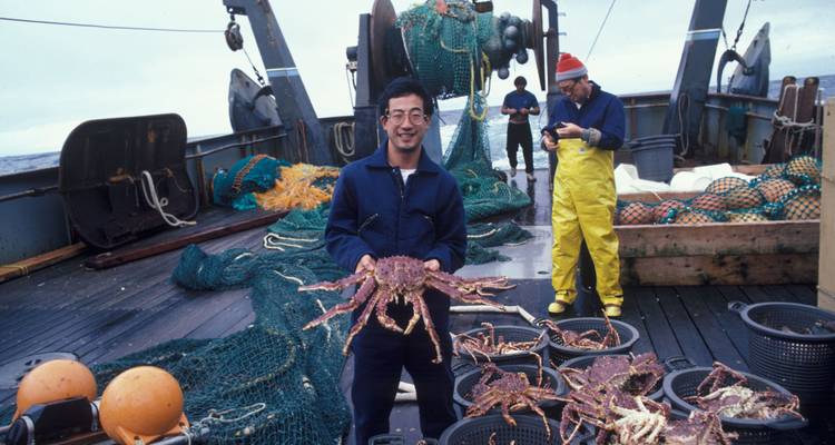 Un pescador mostrando con orgullo un gran centolla en la cubierta de un barco de trabajo en aguas del sur.