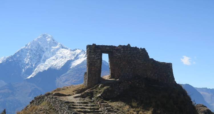 Ruina Inca de piedra encaramada en una cresta con un pico nevado elevándose detrás.