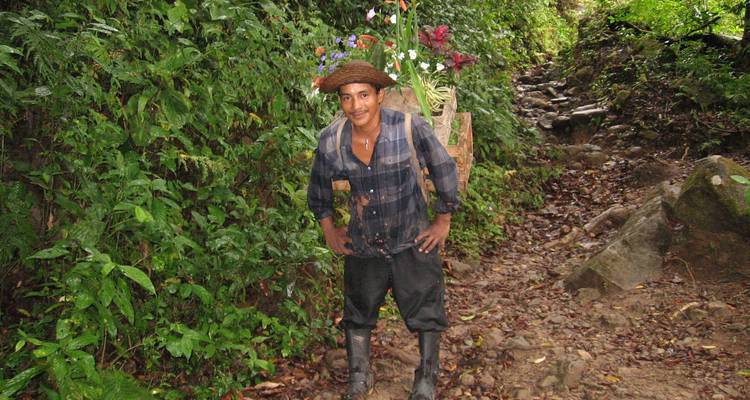 Excursionista sonriente usando botas de goma y cargando plantas en una canasta a lo largo de un sendero pantanoso de la selva.