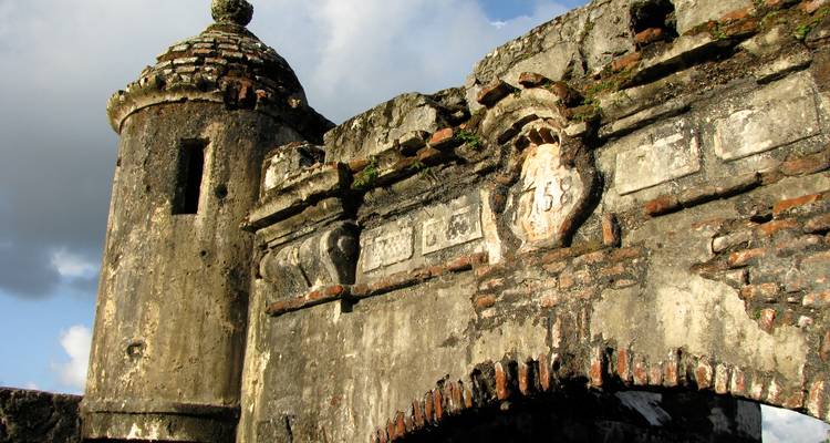 Bastión de piedra desgastada y arco de entrada de un fuerte español antiguo contra un cielo azul.
