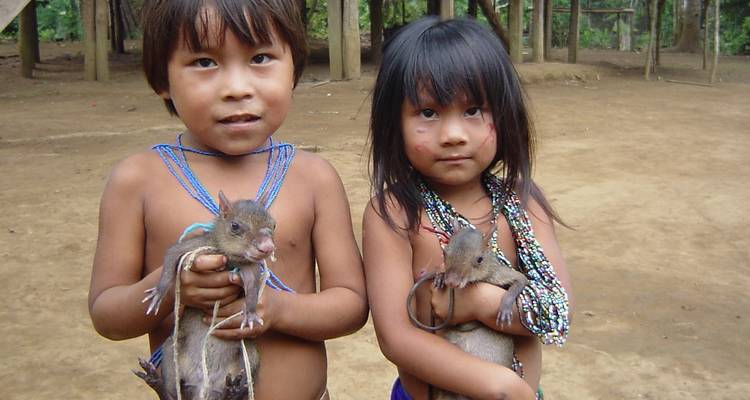 Dos niños indígenas sosteniendo animales pequeños y mirando a la cámara.