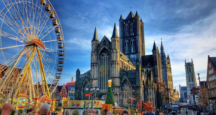 Place festive avec une grande roue à côté d'une imposante église gothique sous un ciel bleu