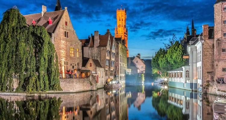 Canal pittoresque bordé de bâtiments de briques médiévales se reflétant dans une eau calme au crépuscule avec la tour du Beffroi illuminée