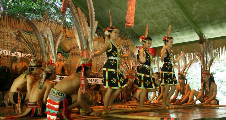 Traditionelle Tänzer aus Sabah in lebendigen Kostümen und gefiederten Kopfschmuck führen auf einer hölzernen Bühne auf.