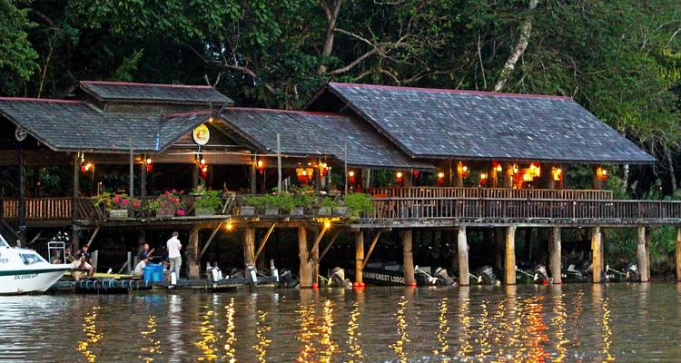 Steifen Sie das Flussufer-Lodges mit Laternenleicht auf, das sich nachts im Wasser spiegelt.