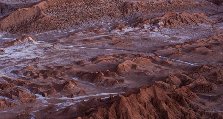 Vue en plongée des formations rocheuses rougeâtres accidentées et des traînées de sel dans le désert d'Atacama.