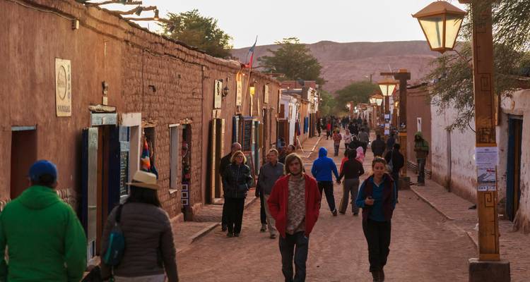 Scène de rue en soirée dans un village en adobe rustique avec des habitants et des touristes se promenant entre les boutiques.