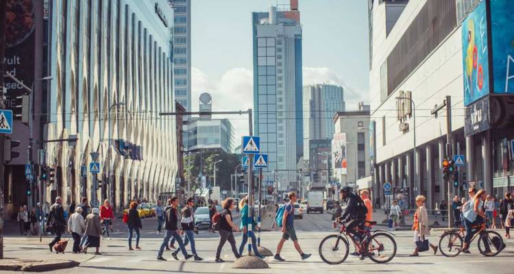 Une intersection urbaine animée avec des piétons et des cyclistes traversant parmi des bâtiments modernes et des feux de circulation.