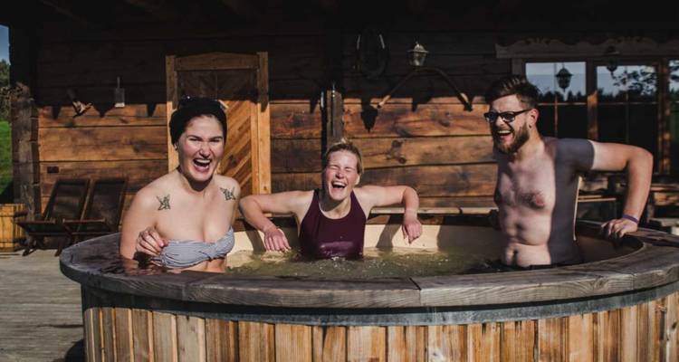 Trois amis rient et se détendent ensemble dans un bain à remous en bois extérieur fumant dans un pavillon rustique.