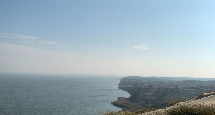 Un horizon de la mer Baltique calme, observé depuis les hautes dunes côtières sous un ciel bleu pâle.