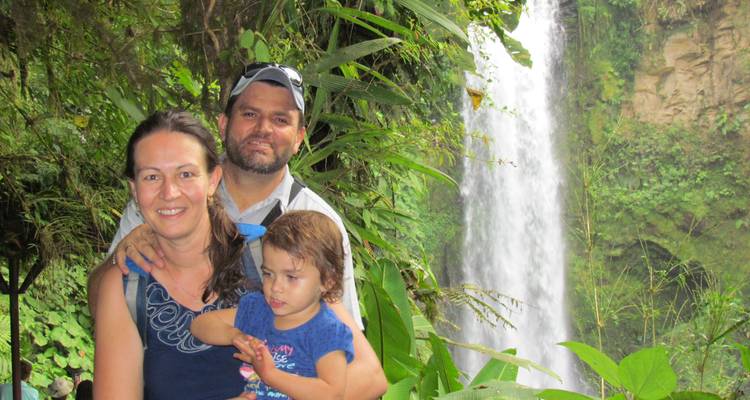 Familia sonriente posando junto a una exuberante cascada de selva tropical