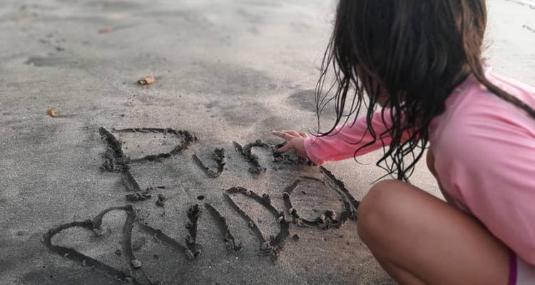 Un niño escribe 'Pura Vida' en la arena mojada de la playa cerca de la orilla