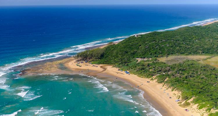 Luchtfoto van een lang zandstrand, turquoise golven en weelderig groen schiereiland langs een afgelegen Afrikaanse kust.