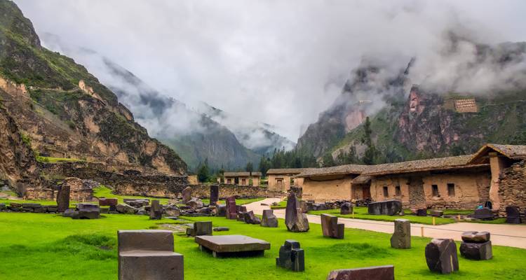 Vallée andine brumeuse avec ruines incas et blocs de pierre dispersés à Ollantaytambo.