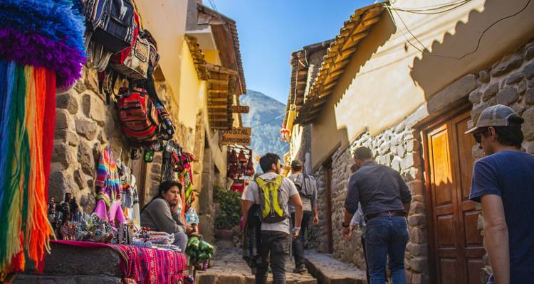 Ruelle étroite en pierre à Ollantaytambo bordée de petits commerces d'artisans colorés et de voyageurs marchant en montée.