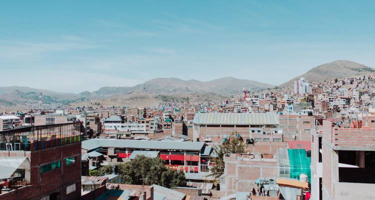 Vue panoramique du paysage urbain de Puno s'étendant sur les collines arides des Andes sous un ciel bleu dégagé.