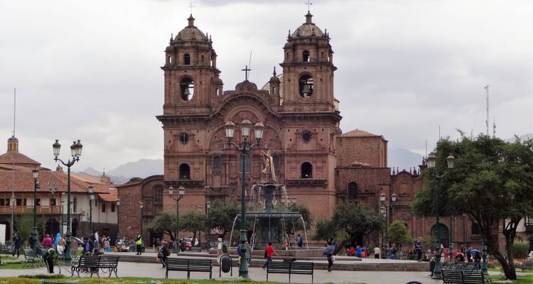 Église historique aux deux clochers dominant une place animée et une fontaine à Cusco.