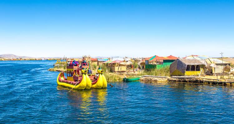 Un bateau traditionnel en roseaux transportant des visiteurs parmi les îles flottantes d'Uros sur les eaux bleues du lac Titicaca.