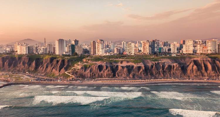 Vue aérienne au coucher de soleil des falaises de Miraflores à Lima et de la skyline moderne au-dessus des vagues du Pacifique.