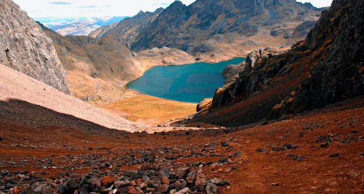 Une vallée andine spectaculaire avec un lac alpin turquoise encadré par des pics escarpés et une pente rocheuse au premier plan.