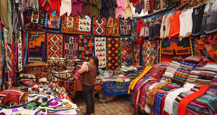 Un étal de marché textile péruvien vibrant débordant de tissus colorés et d'articles artisanaux tandis qu'un client parcourt les produits.