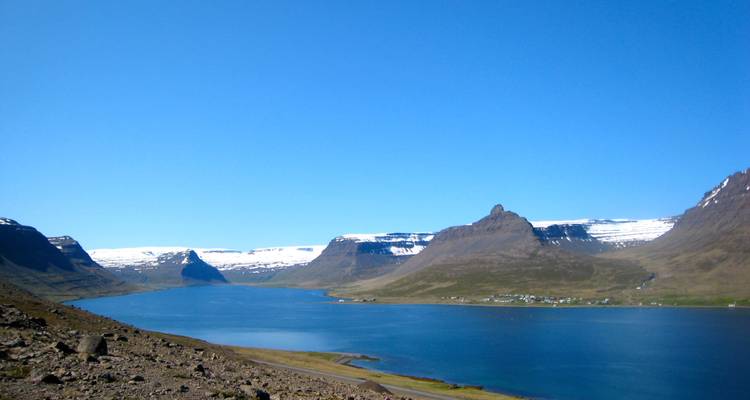 Fjord serein entouré de montagnes zébrées de neige et petit établissement situé sous un ciel bleu cristallin.