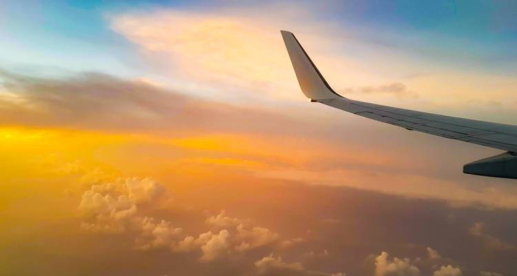 Ala de avión recortada contra un cielo de atardecer vibrante en naranja y azul sobre las nubes