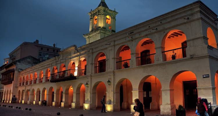 El edificio del Cabildo colonial iluminado brilla en color naranja contra el cielo nocturno en la plaza principal de Salta.