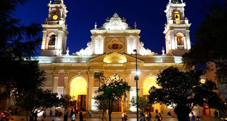 La fachada ornamentalmente iluminada de la catedral barroca de Salta brilla contra el profundo cielo nocturno azul.