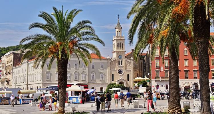 Place animée à Split bordée de palmiers, de bâtiments historiques et d'une activité de rue dynamique.