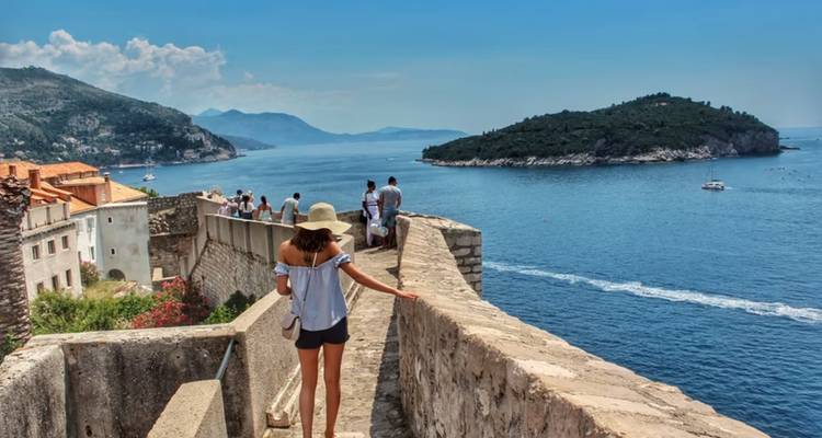Les visiteurs se promènent le long des anciens remparts de Dubrovnik surplombant la mer Adriatique et l'île verdoyante à proximité.