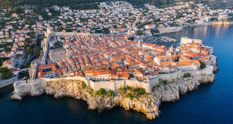 Large panorama aérienne de la péninsule fortifiée de Dubrovnik entourée par une mer bleu profond.