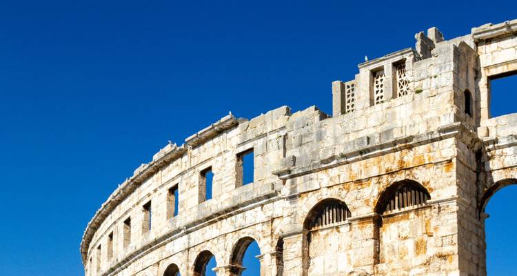 Les arches de pierre de l'ancien amphithéâtre romain de Pula contrastant avec un ciel bleu clair.