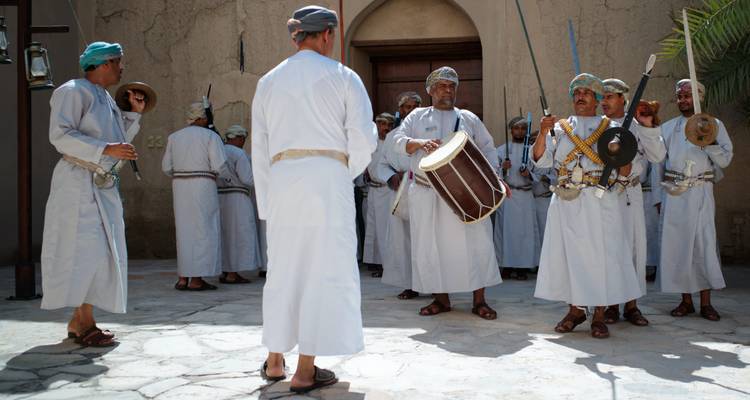 Hombres vistiendo ropa tradicional omaní tocando tambores y blandiendo espadas durante una presentación en el patio.