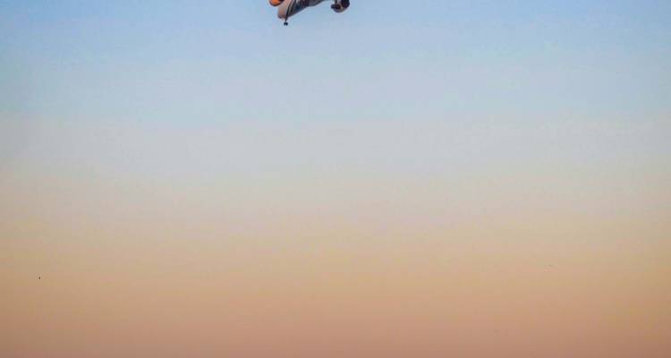 Una pequeña aeronave recortada contra un cielo de atardecer en tonos pastel.
