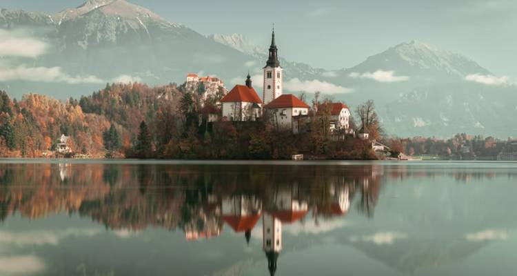 Église emblématique sur l'île du lac de Bled parfaitement reflétée dans les eaux calmes avec les pics alpins en arrière-plan