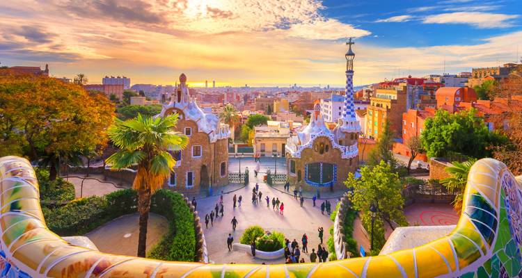 Vue d'un coucher de soleil coloré sur Barcelone depuis la terrasse en mosaïque du parc Güell avec des visiteurs en bas.