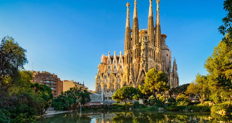 La basilique emblématique de la Sagrada Família reflétée dans un étang sous le ciel bleu clair de Barcelone.